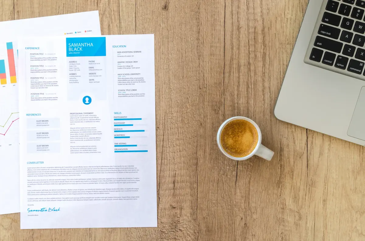 Top view of a desk with resume, coffee cup, and laptop on a wooden surface, ideal for business concepts.