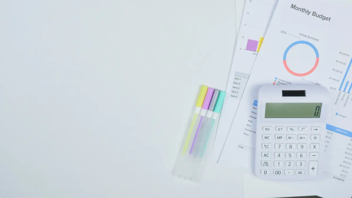Minimalist office desk with a calculator, budget planning documents, and colorful pens.
