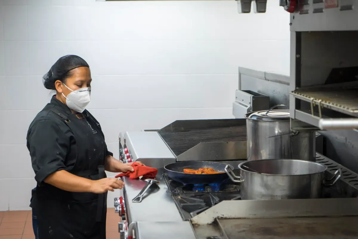 Chef busy at work in a commercial kitchen, preparing dishes while wearing a protective mask.