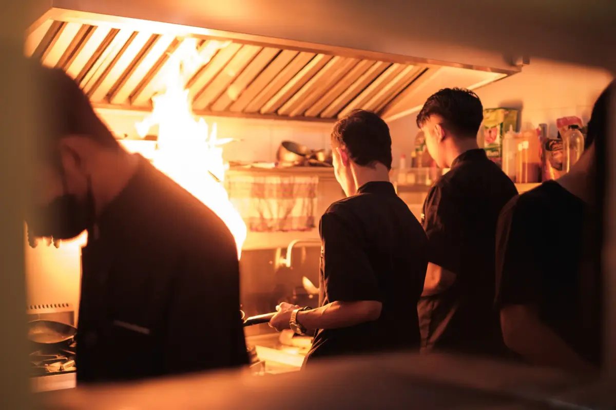 Professional chefs working in a busy industrial kitchen with visible flames.