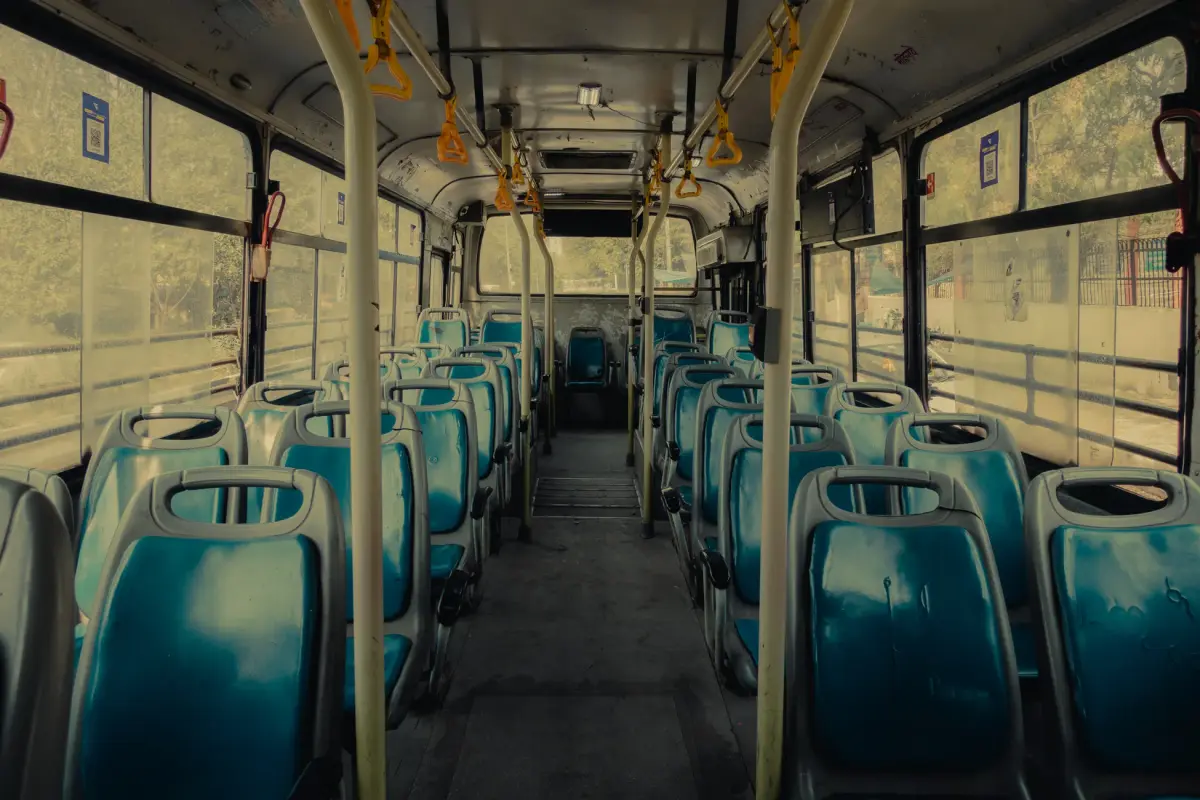 View of an empty public bus interior with blue seats and yellow handrails.