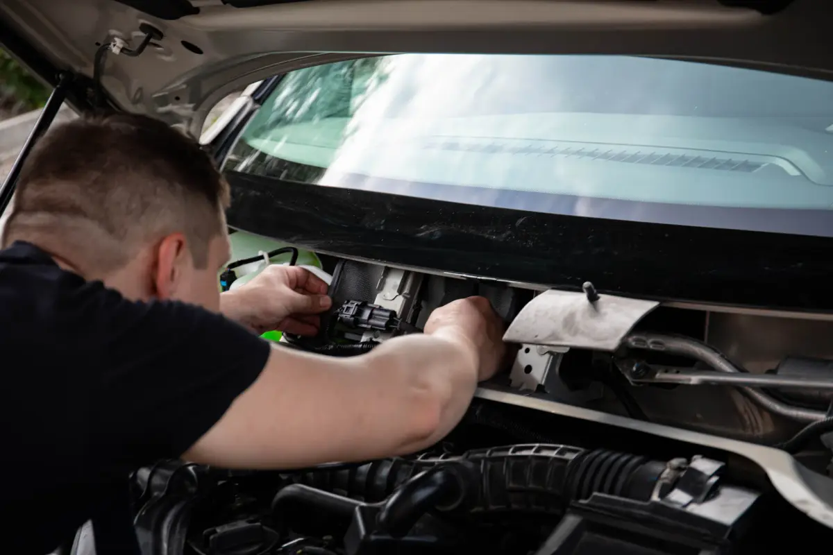 A mechanic working on a car's engine bay indoors, showcasing repair work.