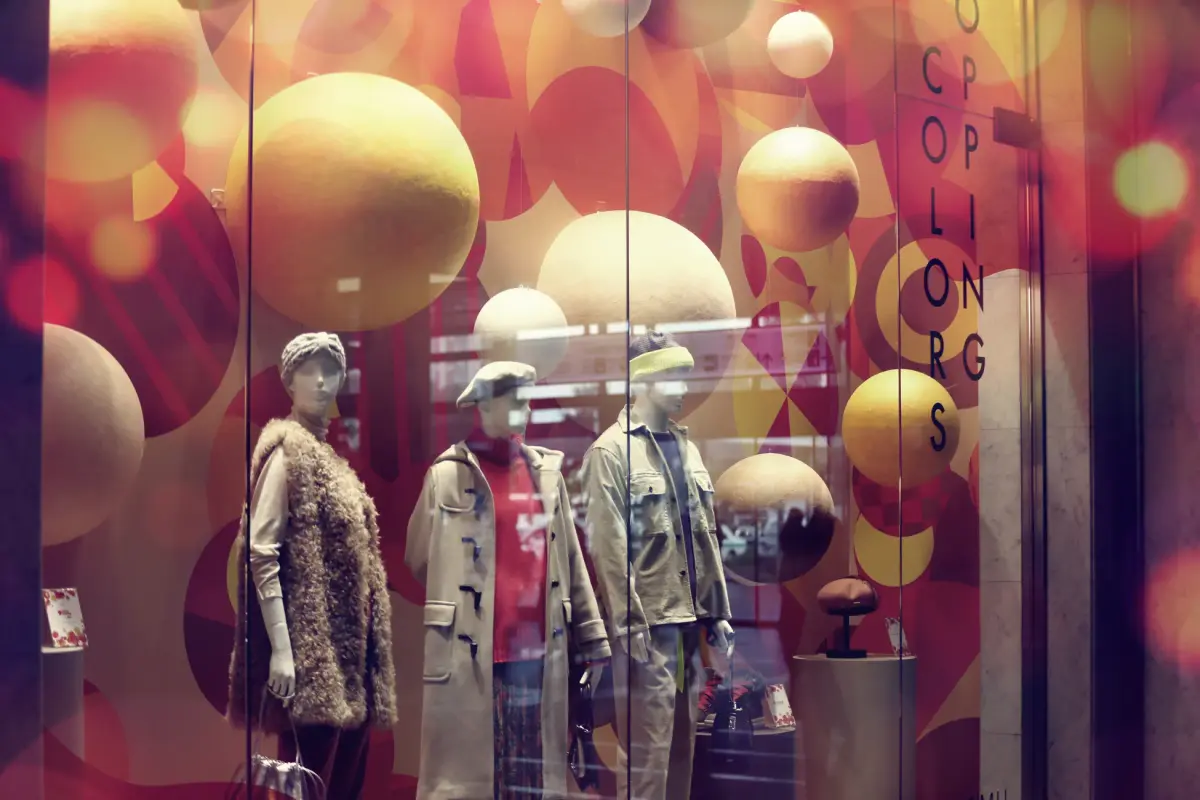 Stylish window display with trendy outfits on mannequins, vibrant design.