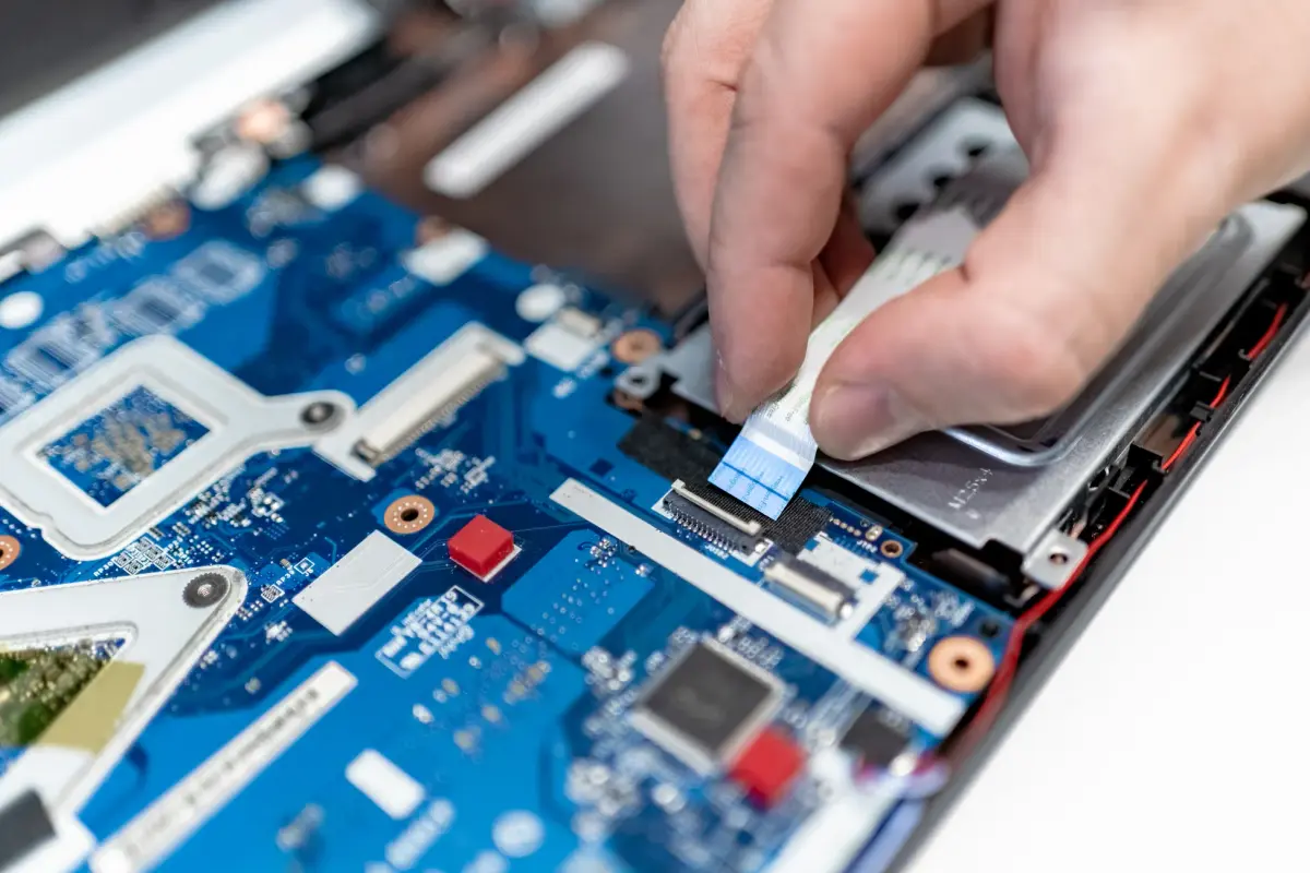 Close-up image of hands repairing a laptop circuit board showing intricate details of electronics.