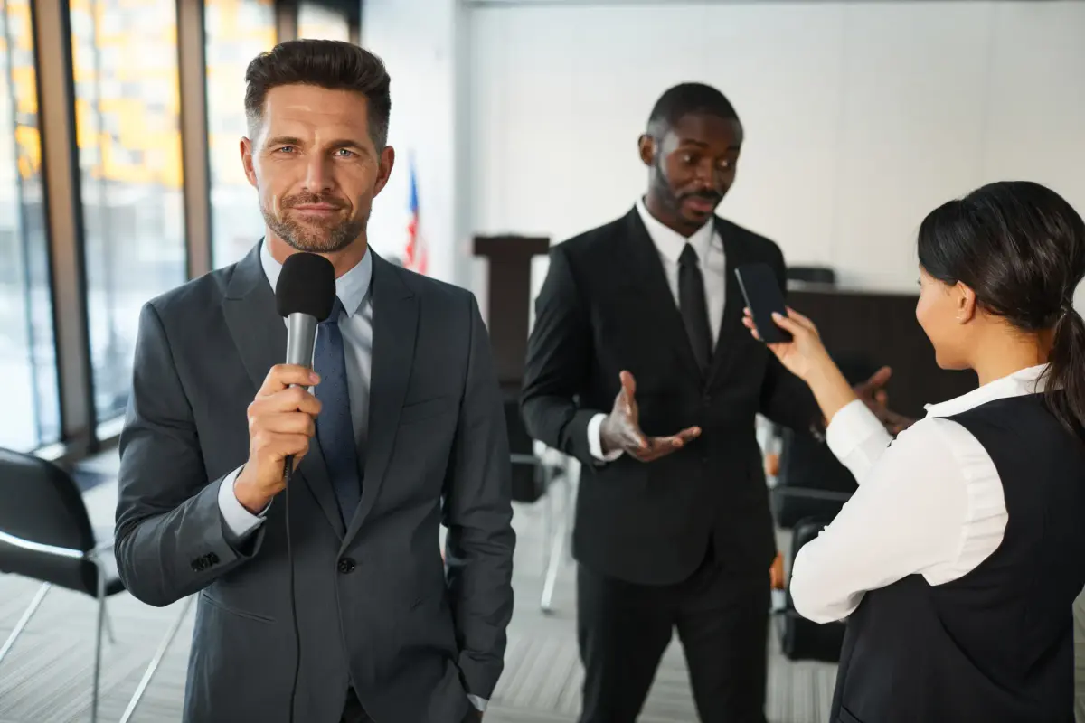 A journalist interviews a businessman in a conference room, capturing a professional and political setting.