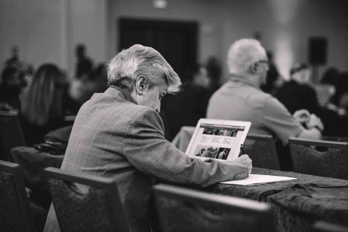 A senior journalist takes notes during a conference, engrossed in thought.