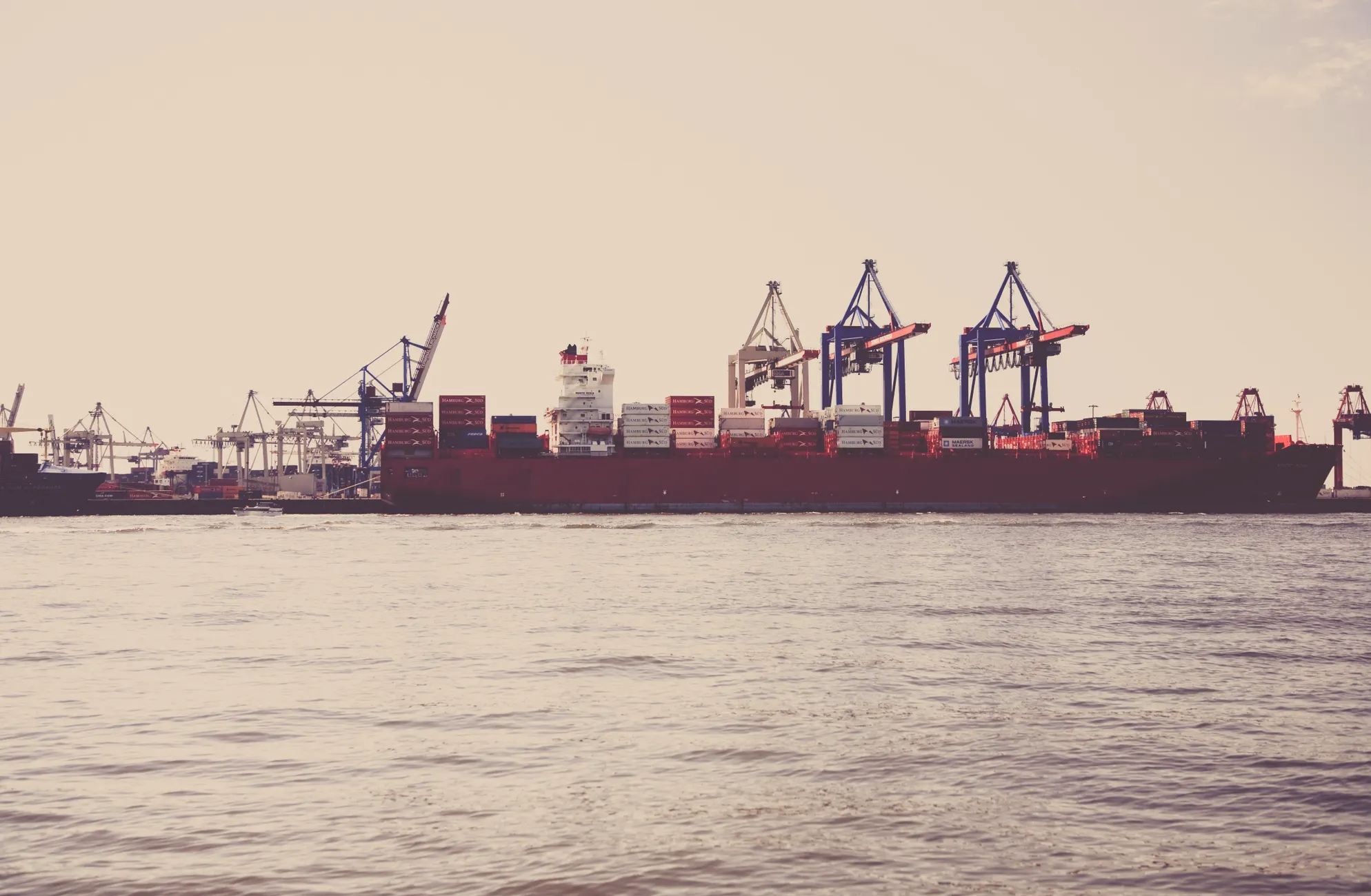 A cargo ship loaded with containers docked at a seaport under clear skies.