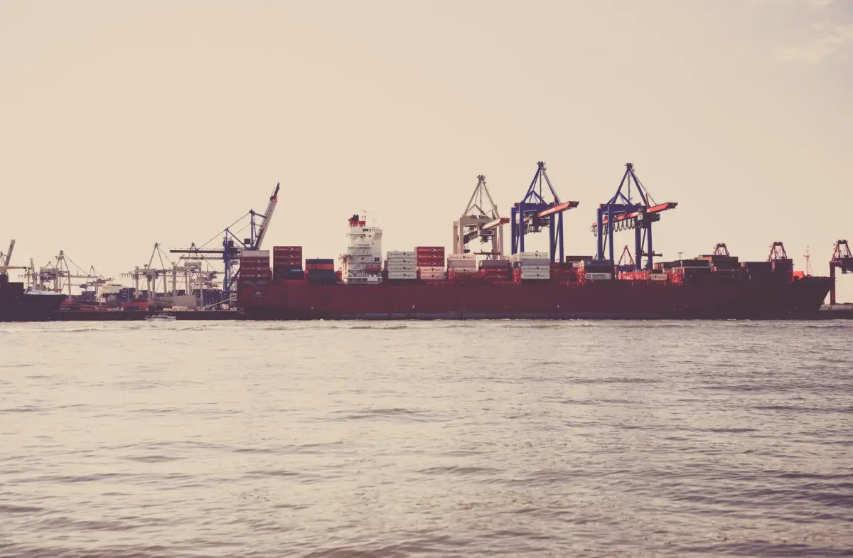 A cargo ship loaded with containers docked at a seaport under clear skies.