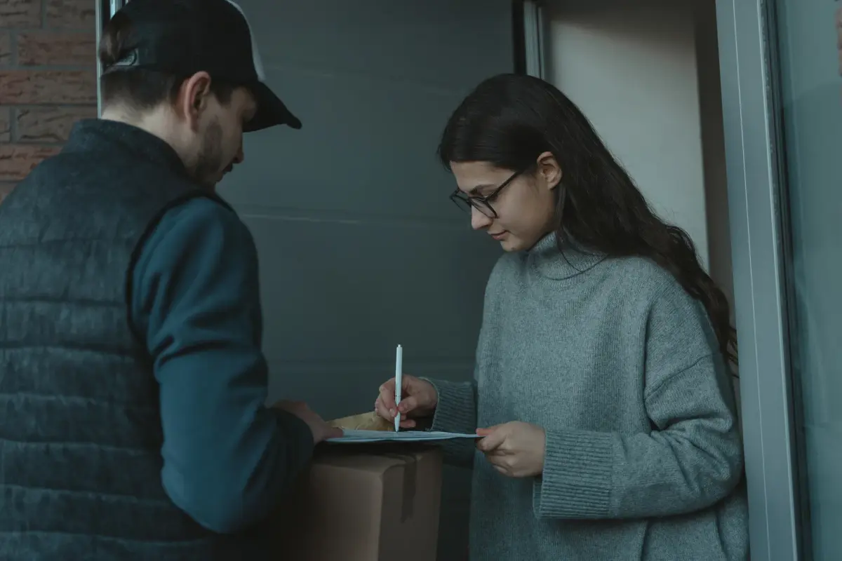 A woman signs for a package delivered by a courier at her doorstep, showcasing home delivery service.
