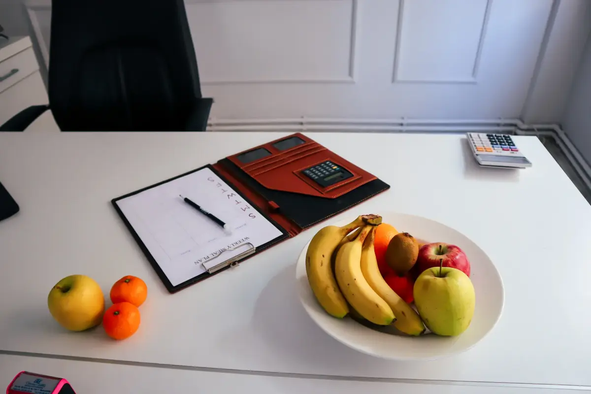 A neat office desk setup with fresh fruits, a planner, and a calculator for organized work days.
