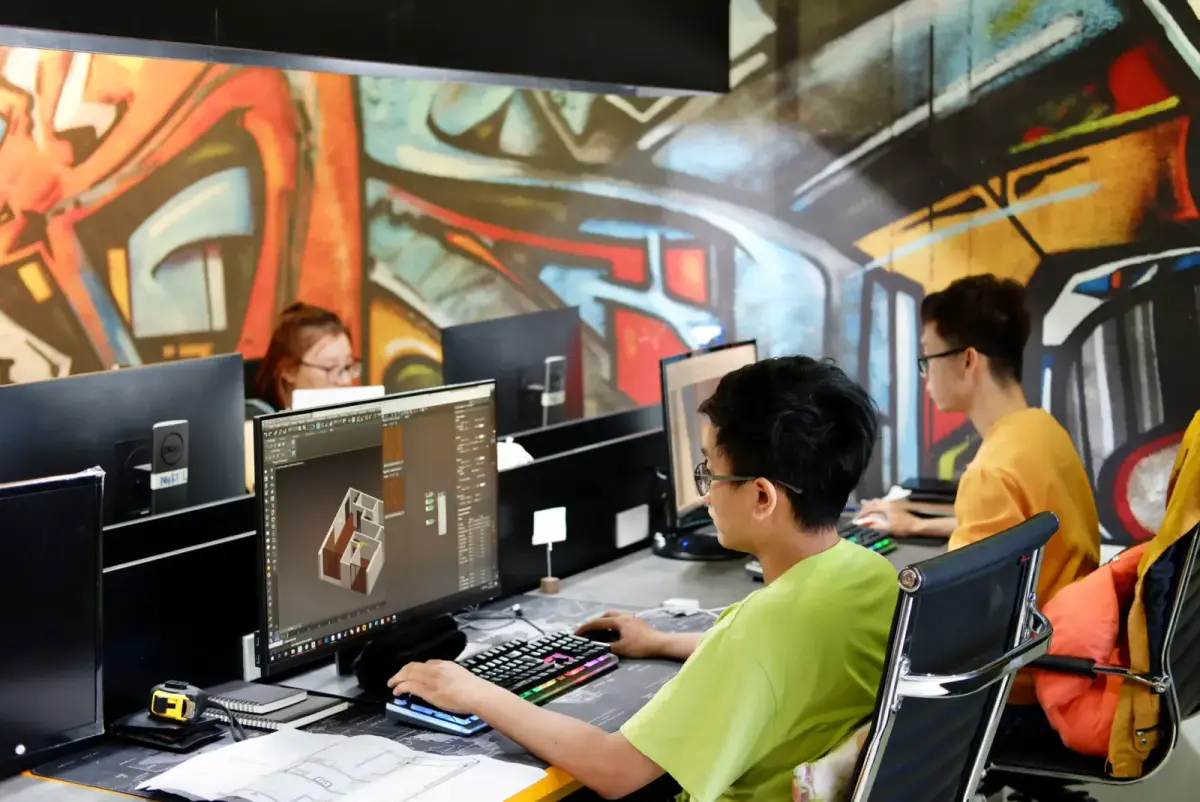 Three young people working on computers in a creative office with vibrant graffiti walls.
