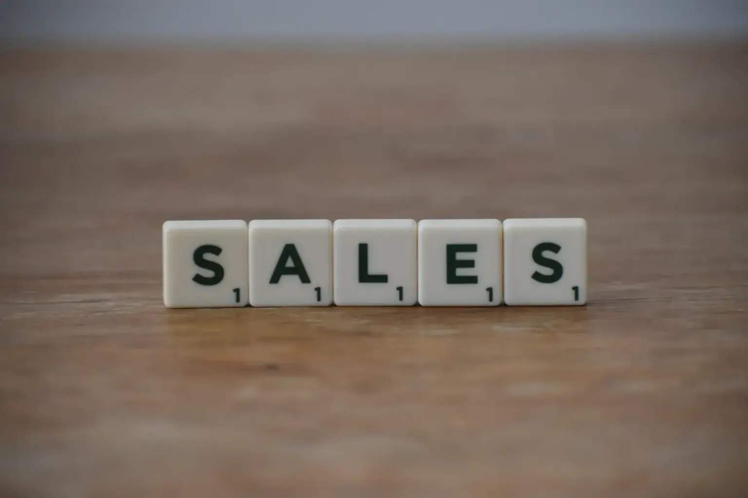 Scrabble tiles spelling 'sales' on a wooden table, emphasizing business and marketing.